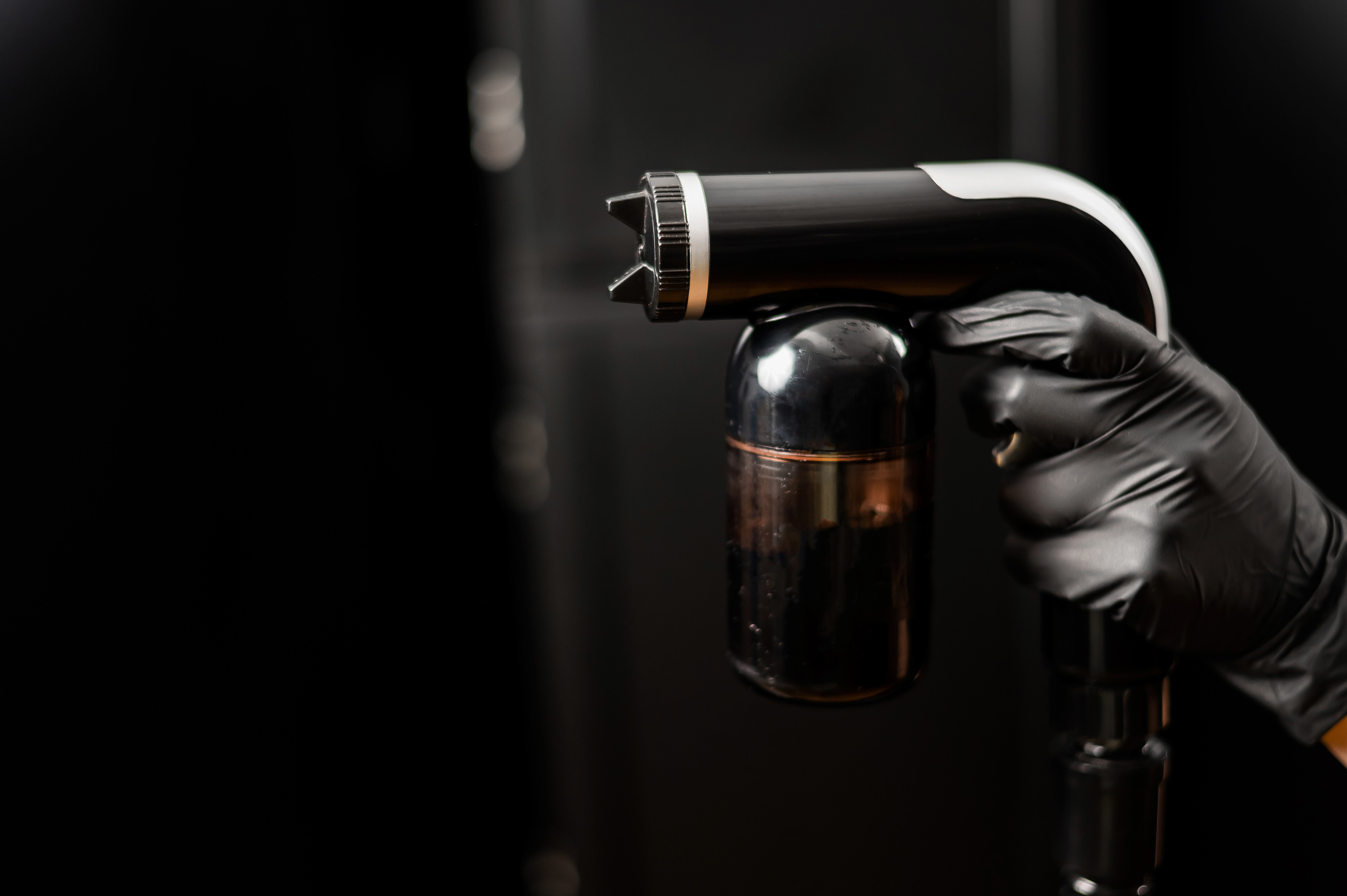 Close-up of Instant Tanning Equipment in the Hands of a Master. Gun Spraying Paint for Leather against Black Background